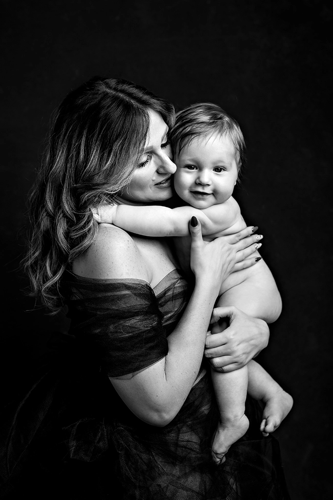 Foto ritrattistica in bianco e nero di una mamma con il bambino nudo in braccio mentre lei lo guarda e lui guarda avnti. Fotografia ritrattistica in bianco e nero di una mamma con il bambino Trieste