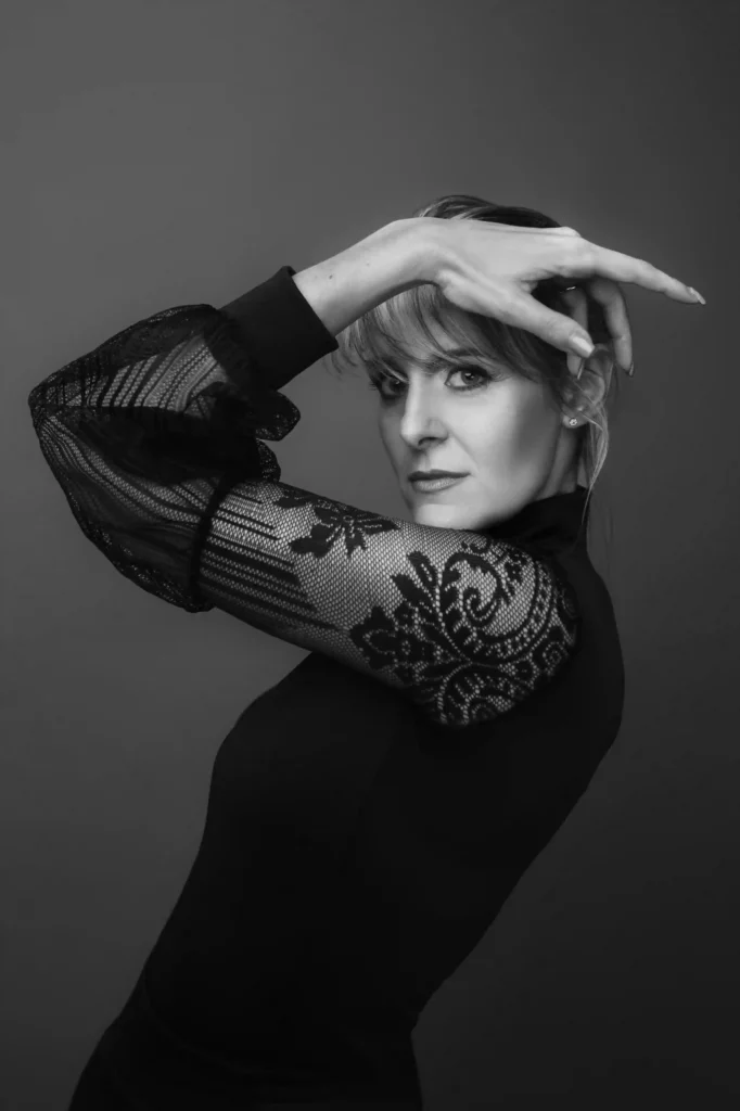 Ritratto in bianco e nero di una donna con le braccia che incorniciano il viso in maniera elegante, con la maglia con le maniche in pizzo. Fotografia donna Trieste