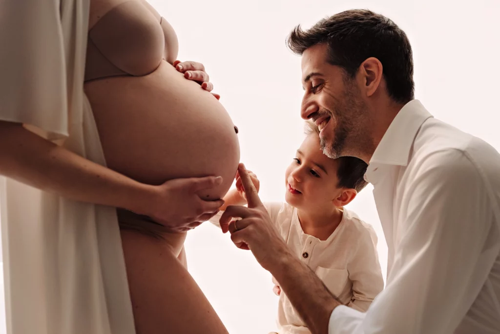 Foto a colori in studio di famiglia, mentre il padre e il bambino toccano la pancia della mamma. Fotografia a colori in studio di famiglia Italia